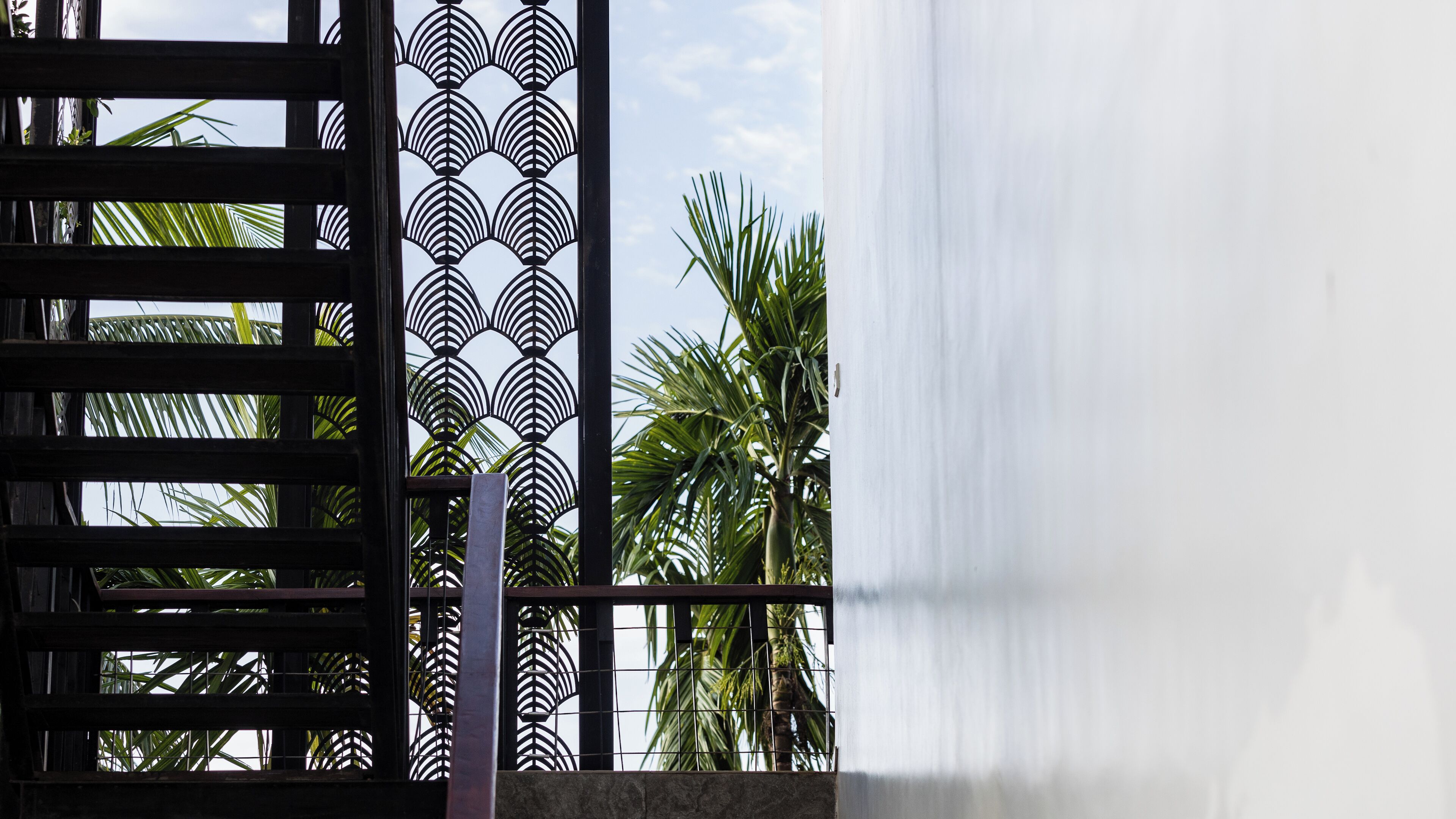 A view through a window with a metal grill, palm trees, and a white curtain.