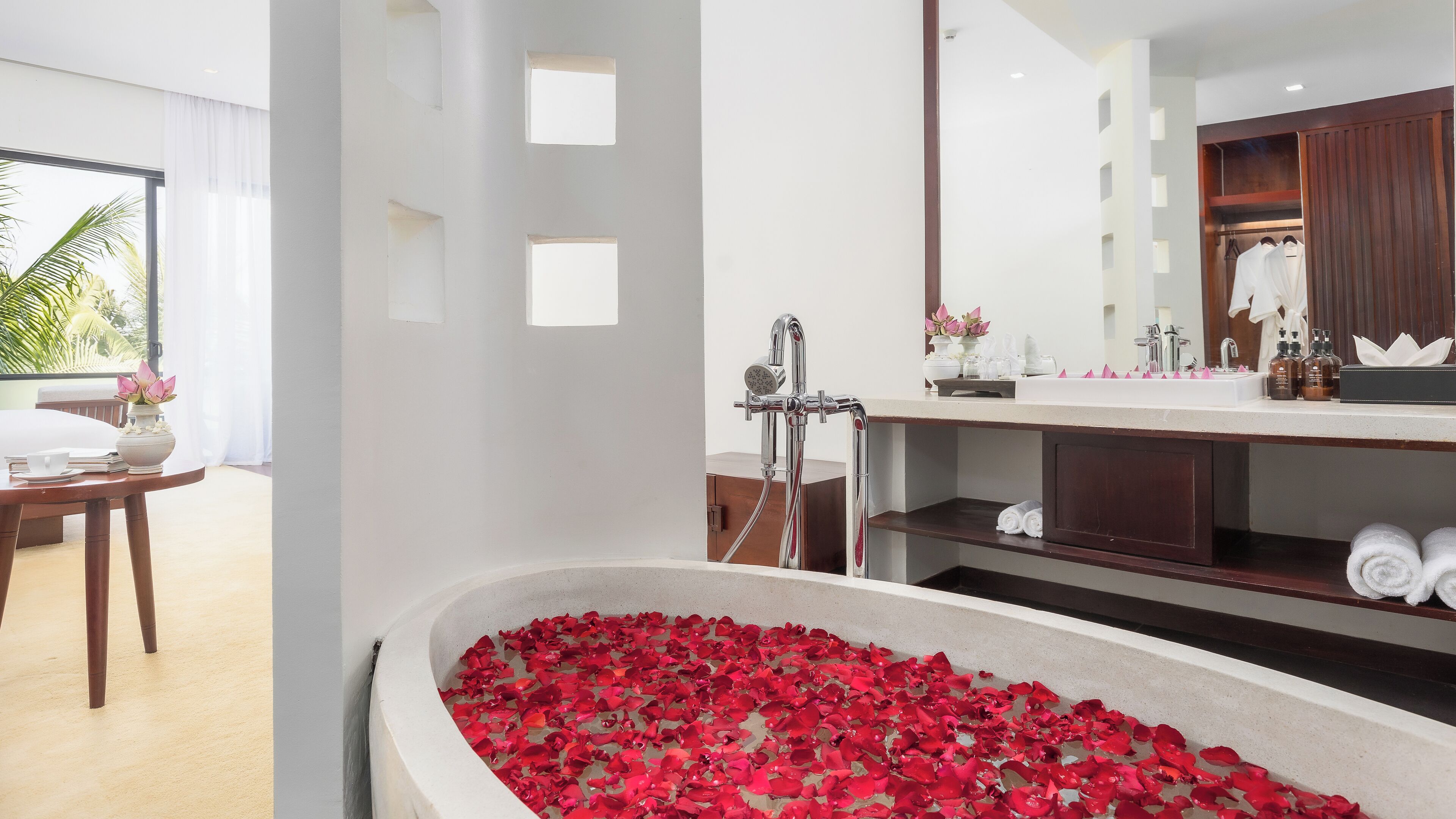 A bathroom with a bathtub filled with rose petals, a sink with toiletries, and a mirror above the sink.