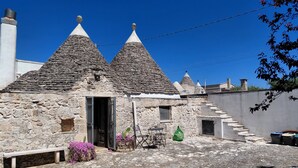 A stone building with conical roofs, a bench, and a cactus plant. - Trullo Genista with Private Pool in the Golden Triangle, Puglia Italy (Martina Franca)