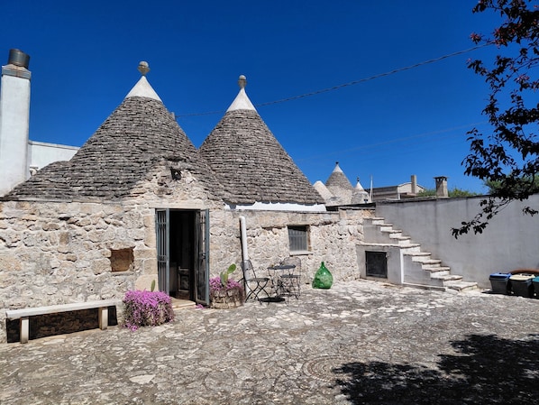 A stone building with conical roofs, a bench, and a cactus plant.