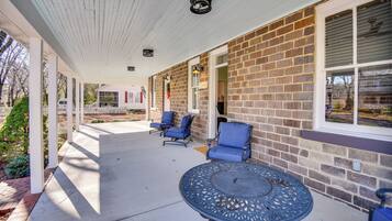 A covered patio with a brick wall, two blue chairs, and a round table.