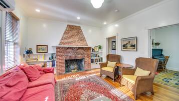 A living room with a brick fireplace, a red sofa, wicker chairs, and a patterned rug.