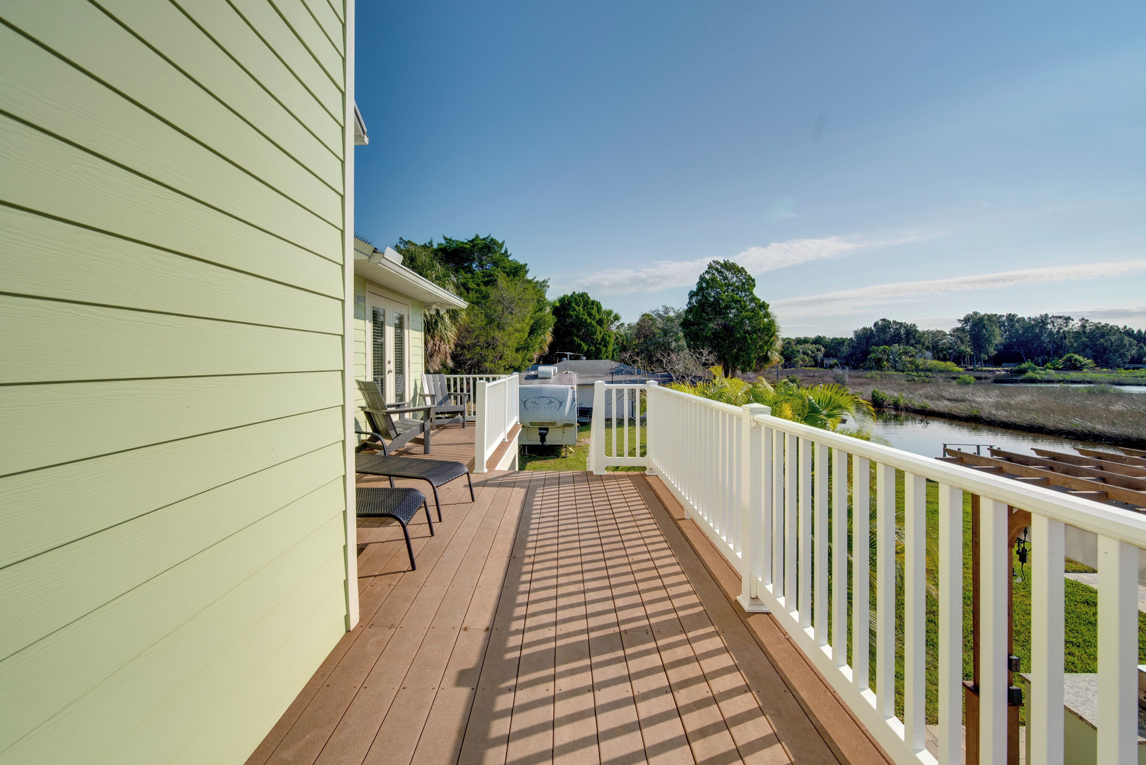 Une terrasse en bois, dotée de mobilier d’extérieur, d’une balustrade blanche et offrant une vue sur une rivière et la verdure environnante.