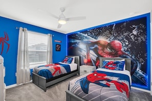 Une chambre avec deux lits, un ventilateur de plafond, une grande fresque représentant Spider-Man et une fenêtre avec des stores.