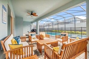 Un espace extérieur abrité, doté de mobilier en bois, d’un ventilateur de plafond et offrant une vue sur une piscine.