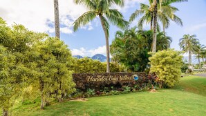 Segnaletica per Hanalei Bay Villas, con un muro in pietra e vegetazione lussureggiante.