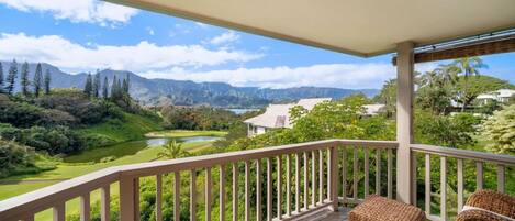 A balcony with a view of a golf course, mountains, and a lake.