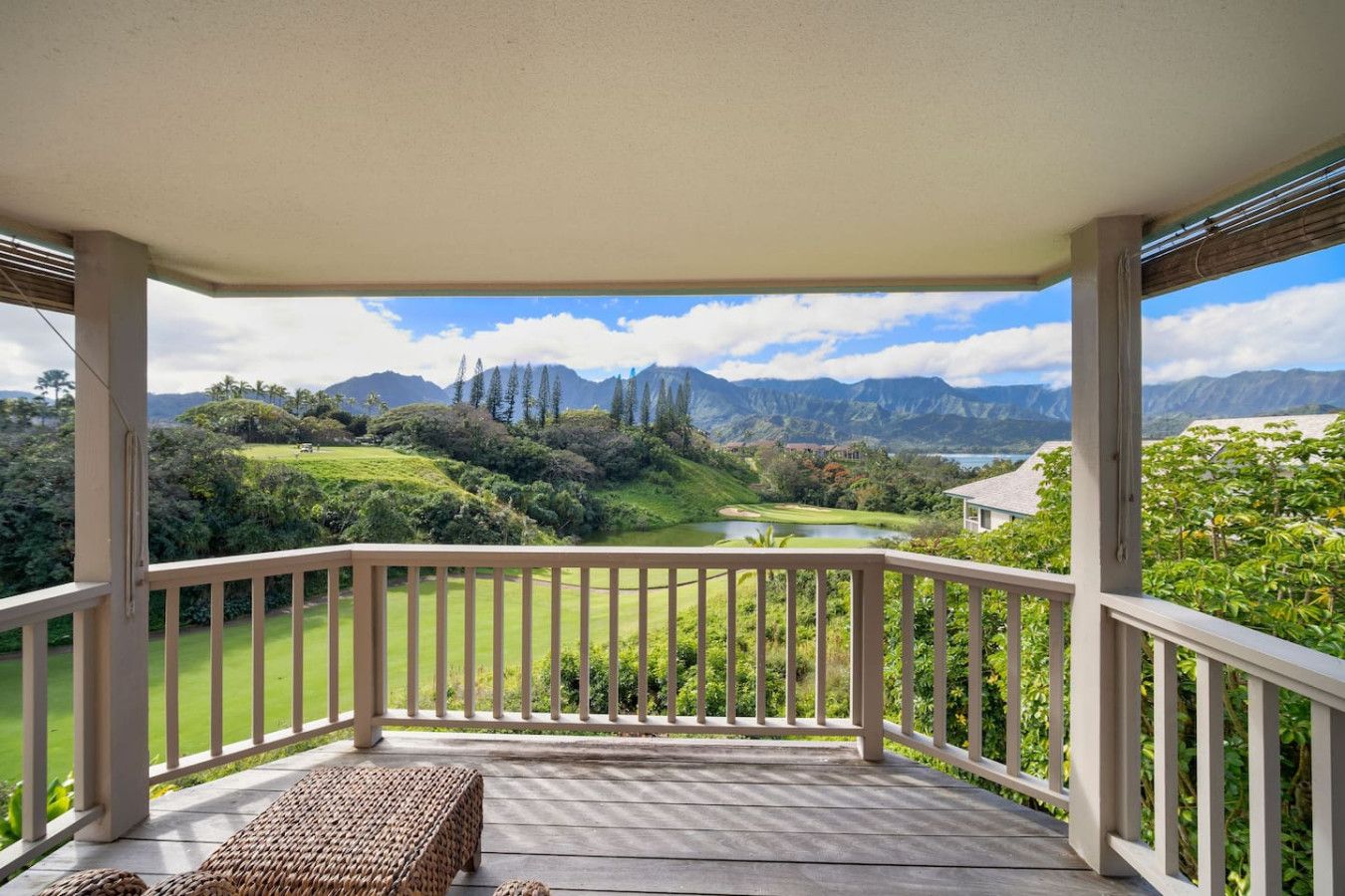 A covered porch with a view of a golf course and mountains.
