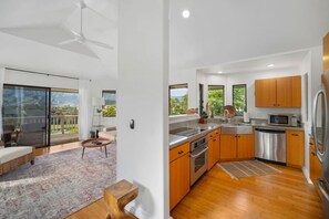 A modern kitchen with wooden cabinets, stainless steel appliances, and a large window overlooking greenery. - Magical views of Hanalei Bay, Napali Coast and the Makai Golf Course in a beautifully styled home (Princeville)