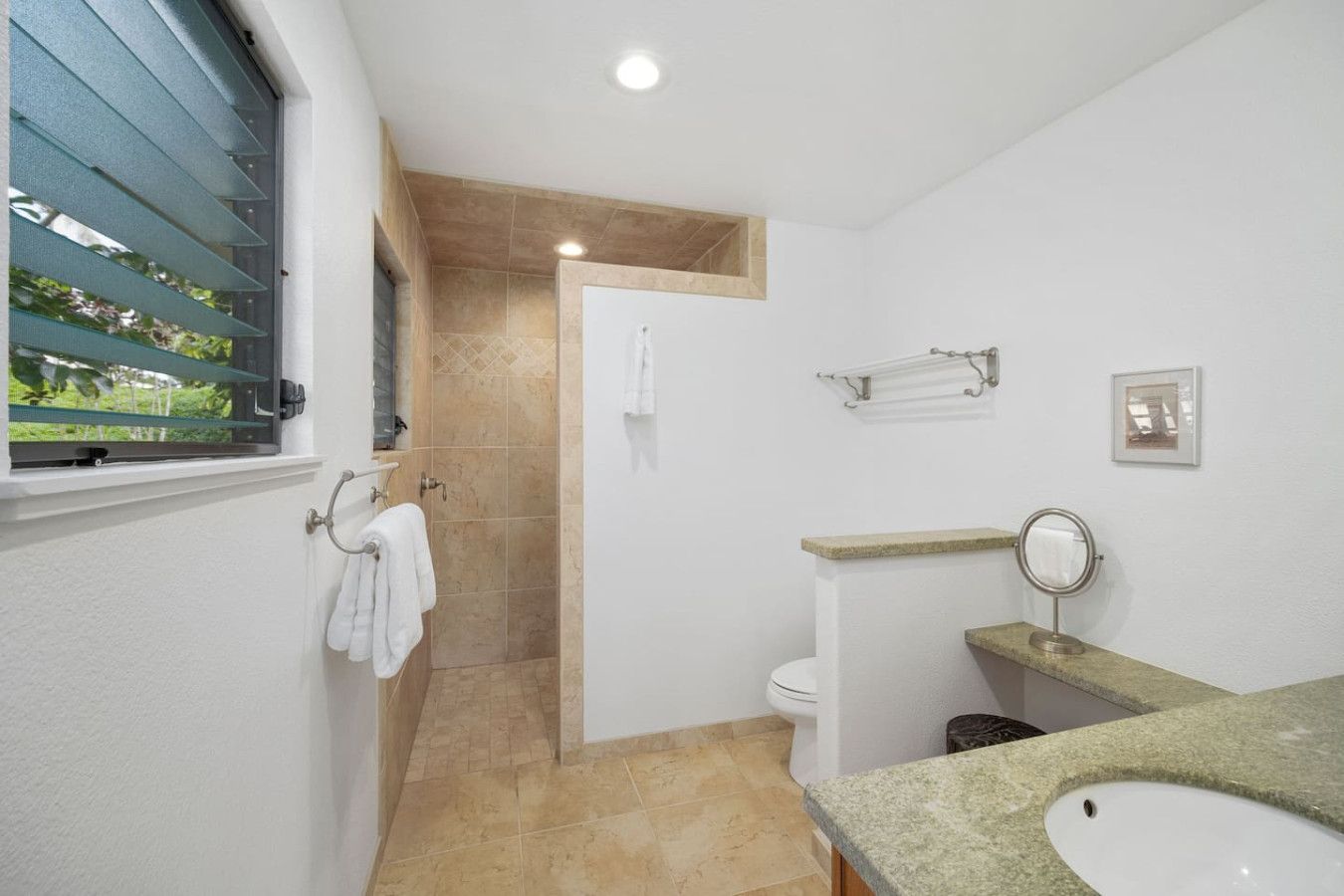 A bathroom with a shower, toilet, sink, and window with blinds.