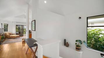 Een ruime woonkamer met houten vloer, een eettafel en een bank. Er is een schuifdeur naar een balkon met planten.
