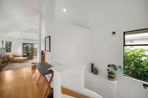 A spacious living area with a wooden floor, a dining table, and a sofa. There is a sliding glass door leading to a balcony with plants. - Magical views of Hanalei Bay, Napali Coast and the Makai Golf Course in a beautifully styled home (Princeville)