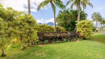 Naamplaatje voor Hanalei Bay Villas, met een stenen muur en weelderige begroeiing.