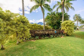 A sign for Hanalei Bay Villas with a stone wall and lush greenery. - Magical views of Hanalei Bay, Napali Coast and the Makai Golf Course in a beautifully styled home (Princeville)