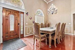 A dining room with a wooden table and chairs, a chandelier, and a stained glass window. - Casa Oasis - Large Home, 1-Acre, Near Trails & Fun (Springdale)