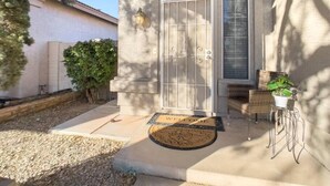 Une maison avec une façade en pierre, une grande entrée en arc de cercle, un paillasson et un petit espace extérieur aménagé avec une chaise et un pot de fleurs.