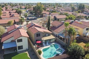 Un quartier résidentiel avec des maisons, une piscine et une terrasse équipée de chaises et de parasols.