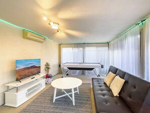 Ein gemütliches Wohnzimmer mit einer Couch, einem kleinen runden Tisch, einem Billardtisch, einem Fernseher und einer Zimmerpflanze.