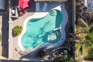 An aerial view of a swimming pool with a unique shape, surrounded by lounge chairs and a red umbrella. - Chandler 3BR | Pool + Game Room | Pet Friendly (Chandler)
