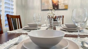 Une table à manger dressée avec de l’assiette blanche, des bols et des verres à vin, et un vase rempli de fleurs blanches placé au centre.