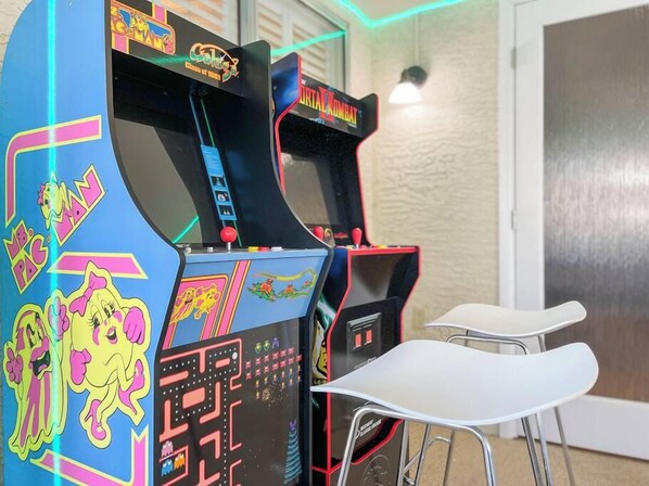Deux bornes d’arcade aux graphismes colorés, avec une chaise blanche au premier plan.