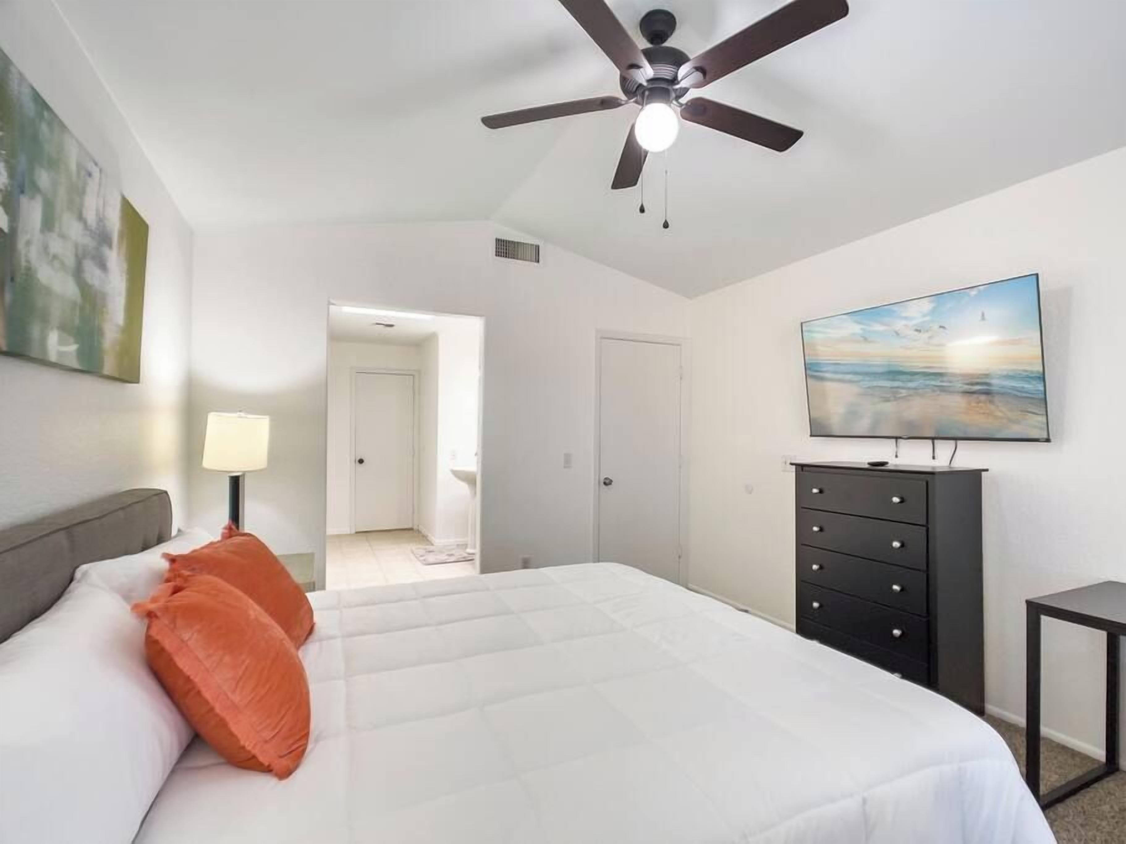 A bedroom with a bed, a ceiling fan, a TV, and a painting on the wall.