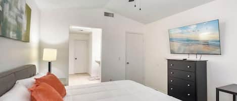 A bedroom with a bed, a ceiling fan, a TV, and a painting on the wall.