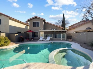 A residential swimming pool with a covered patio area, a barbecue setup, and a large house in the background. - Chandler 3BR | Pool + Game Room | Pet Friendly (Chandler)