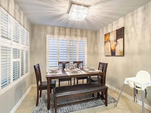 A dining room with a large table set for six, flanked by windows with blinds, a chandelier, and a painting on the wall. - Chandler 3BR | Pool + Game Room | Pet Friendly (Chandler)