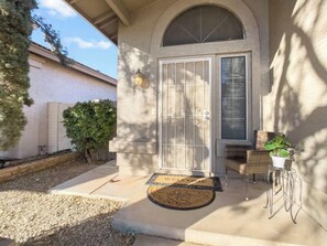 A house with a stone facade, a large arched entrance, a welcome mat, and a small outdoor seating area with a chair and a potted plant.