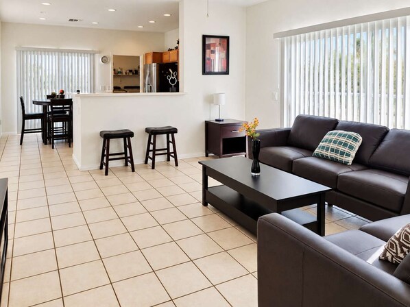 A modern living room with a sofa, coffee table, and a dining area with chairs and a table.