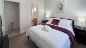 Hotellihuone, jossa on suuri sänky, yöpöytä lampun kanssa, taulu seinällä ja kylpyhuone, joka näkyy avoimesta ovesta.