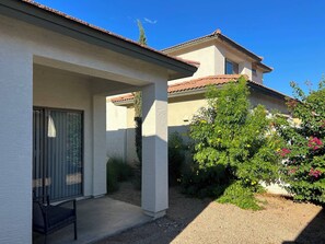 Ein Haus mit überdachter Terrasse, ein Garten mit blühenden Pflanzen und einem strahlend blauen Himmel.