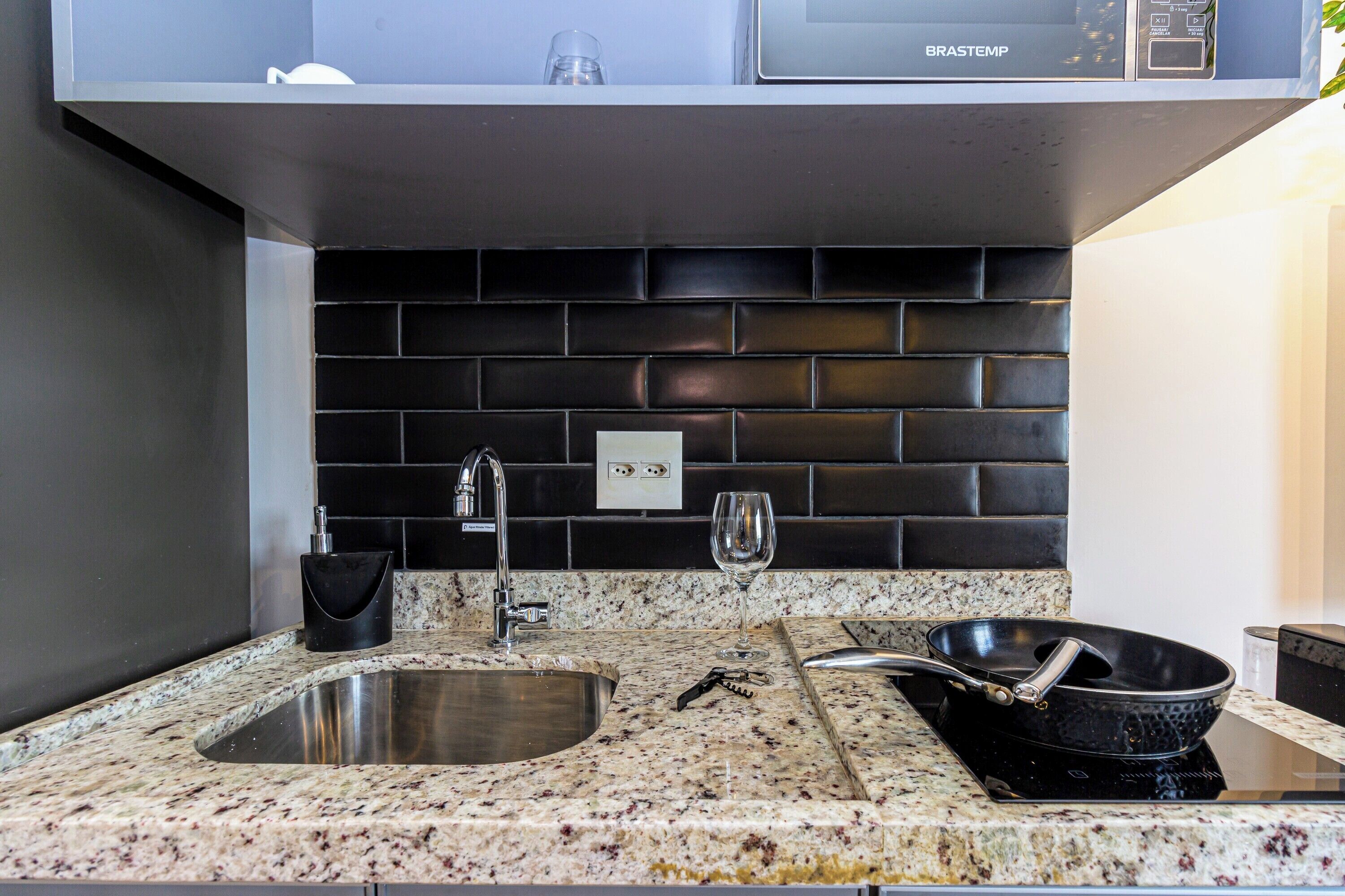 Cocina con encimera de granito, pileta de acero inoxidable y salpicadero negro.