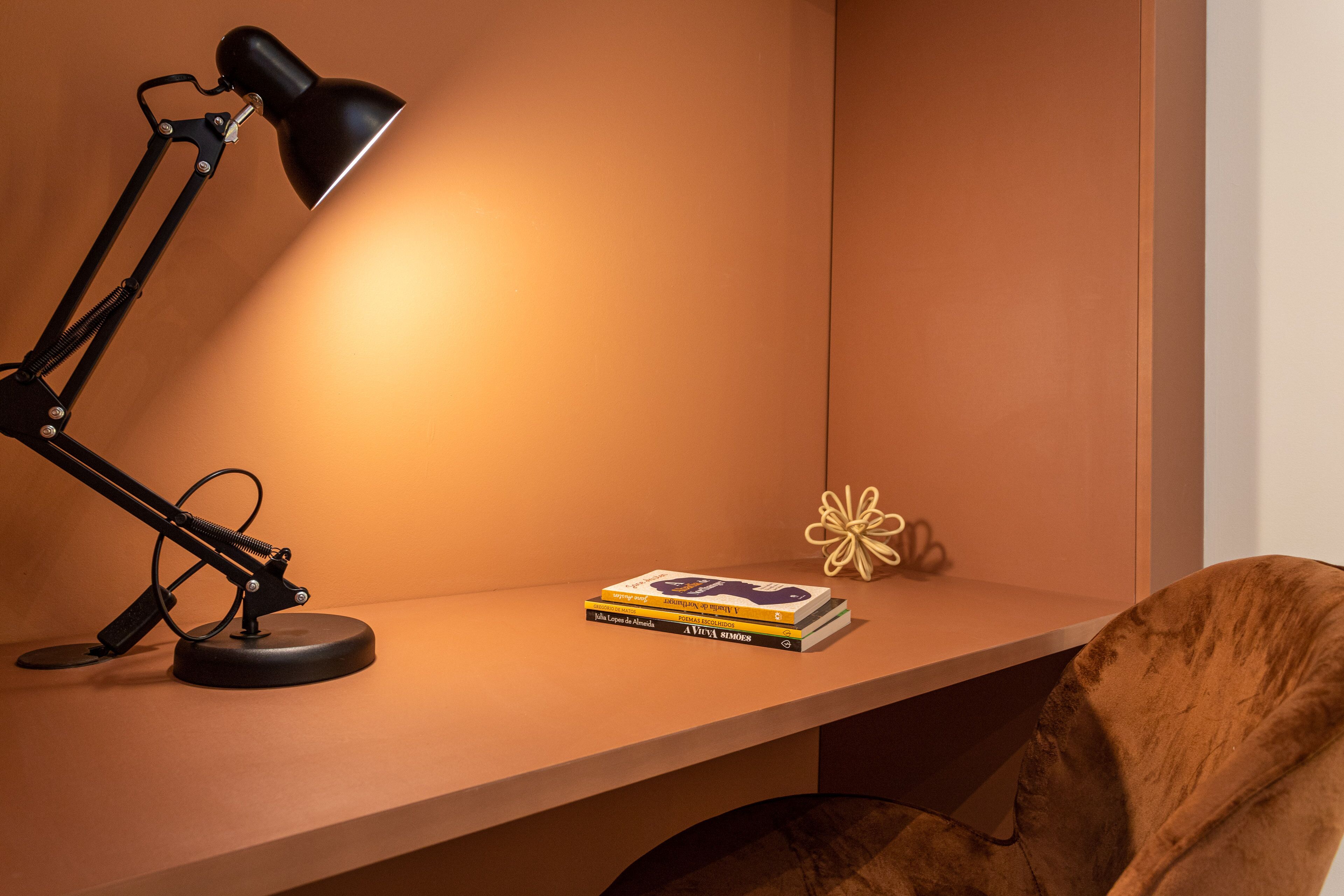 A desk with a desk lamp, a stack of books, and a decorative flower.