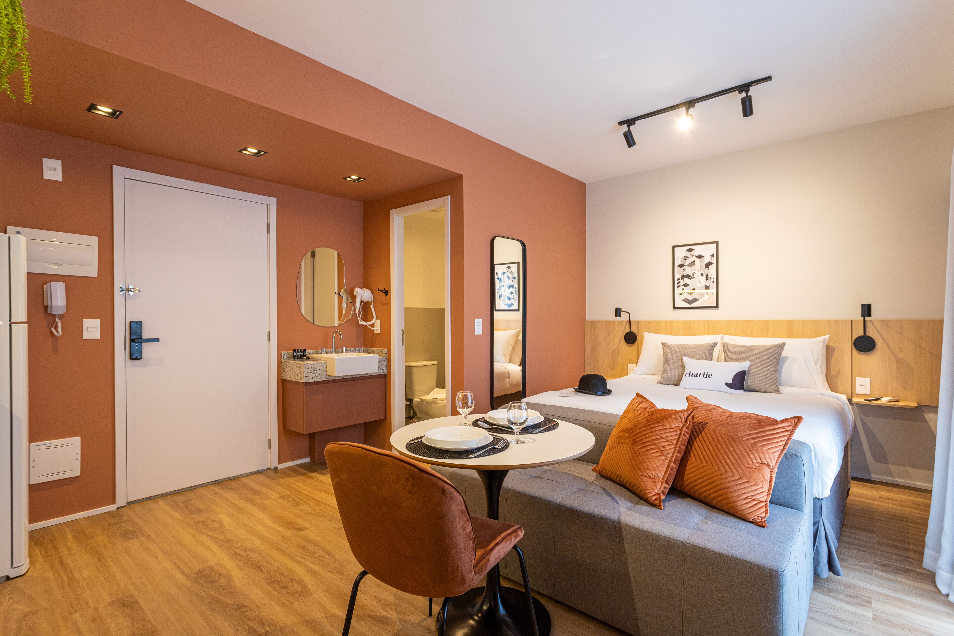 A modern hotel room with a bed, a sitting area with a table and chairs, a bathroom, and a small kitchenette.