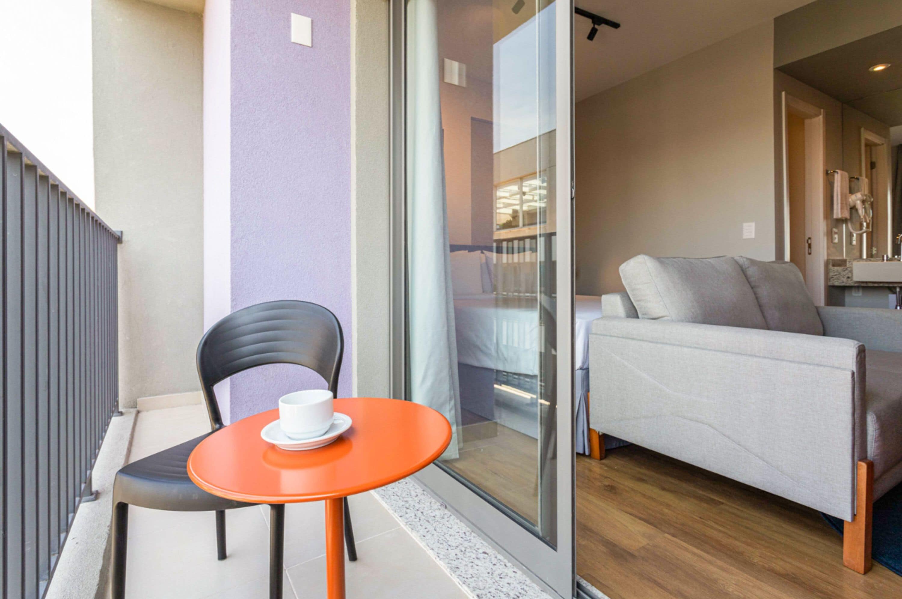 A balcony with a chair and table, a sofa, and a sliding glass door leading to a bedroom.
