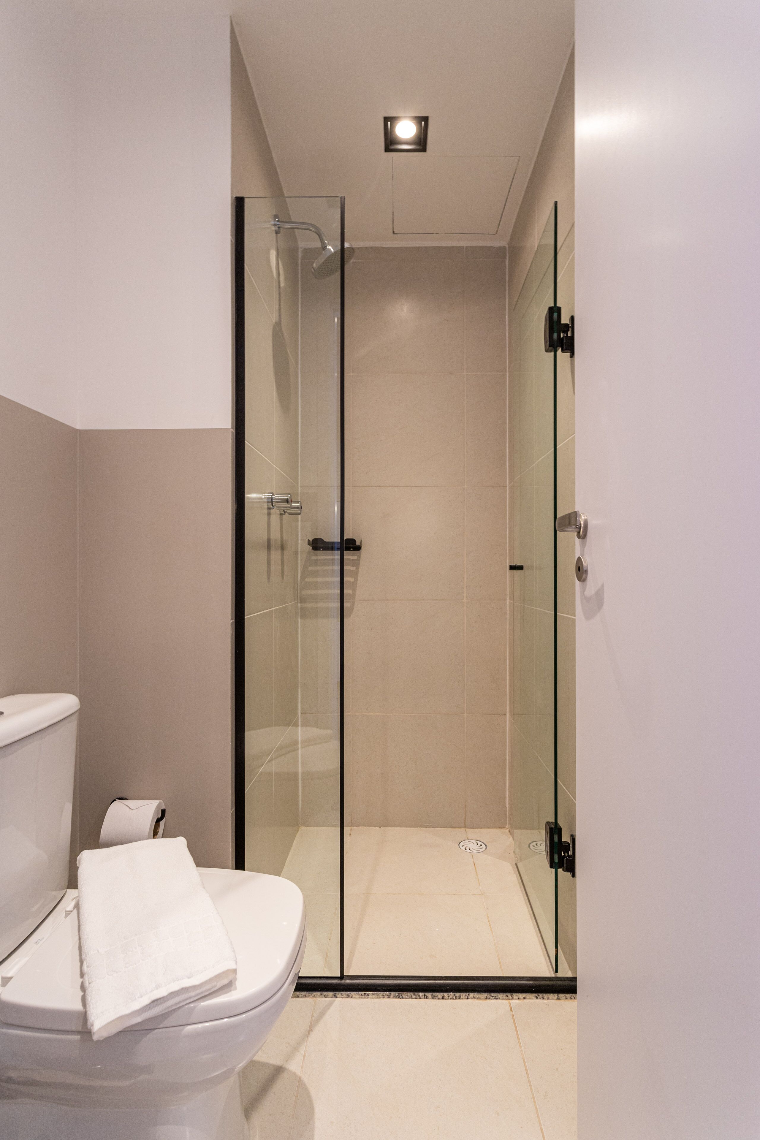 A modern bathroom with a glass-enclosed shower, a toilet, and a towel on the seat.