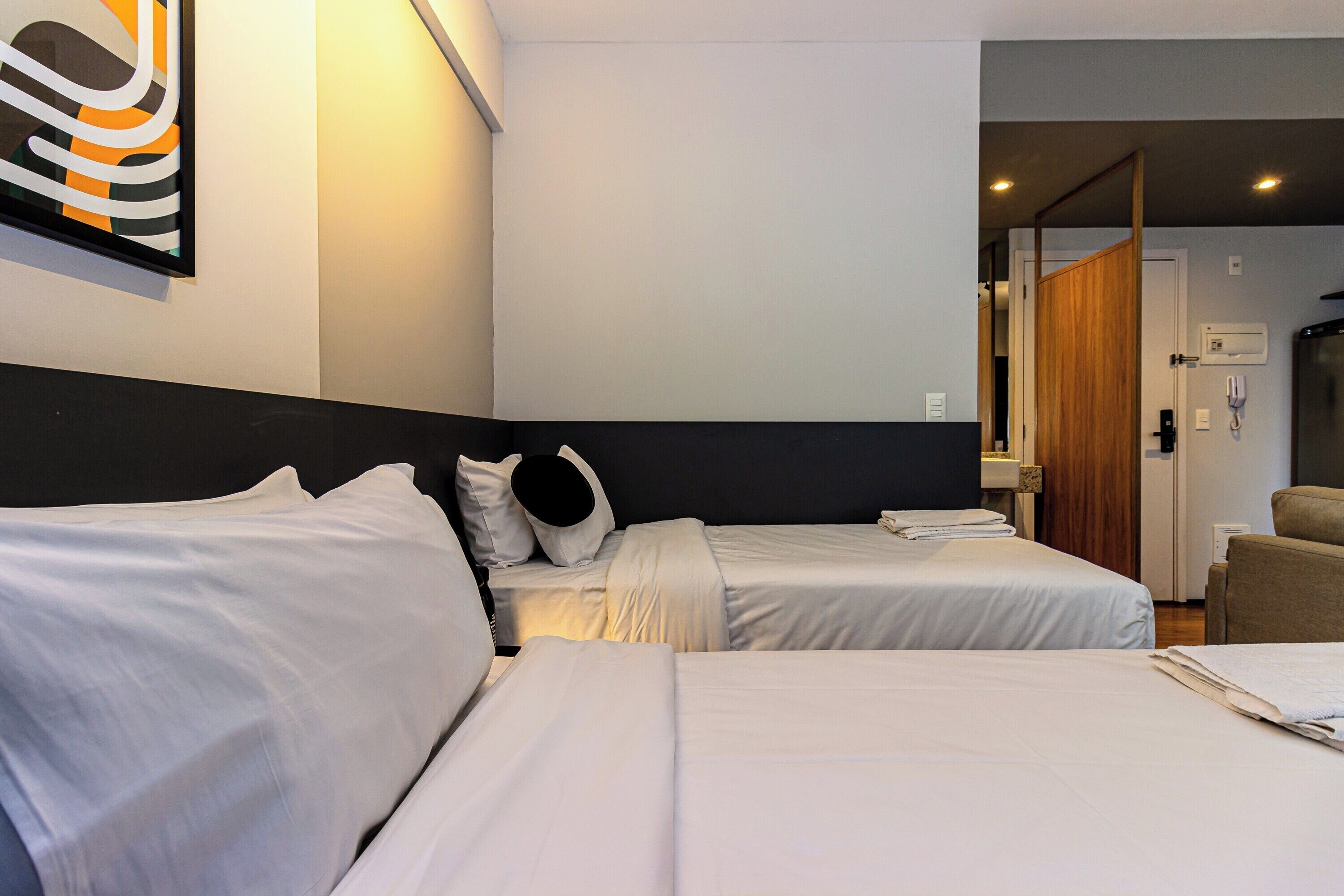 A hotel room with two single beds, a wooden door, a telephone, and a wall-mounted artwork.