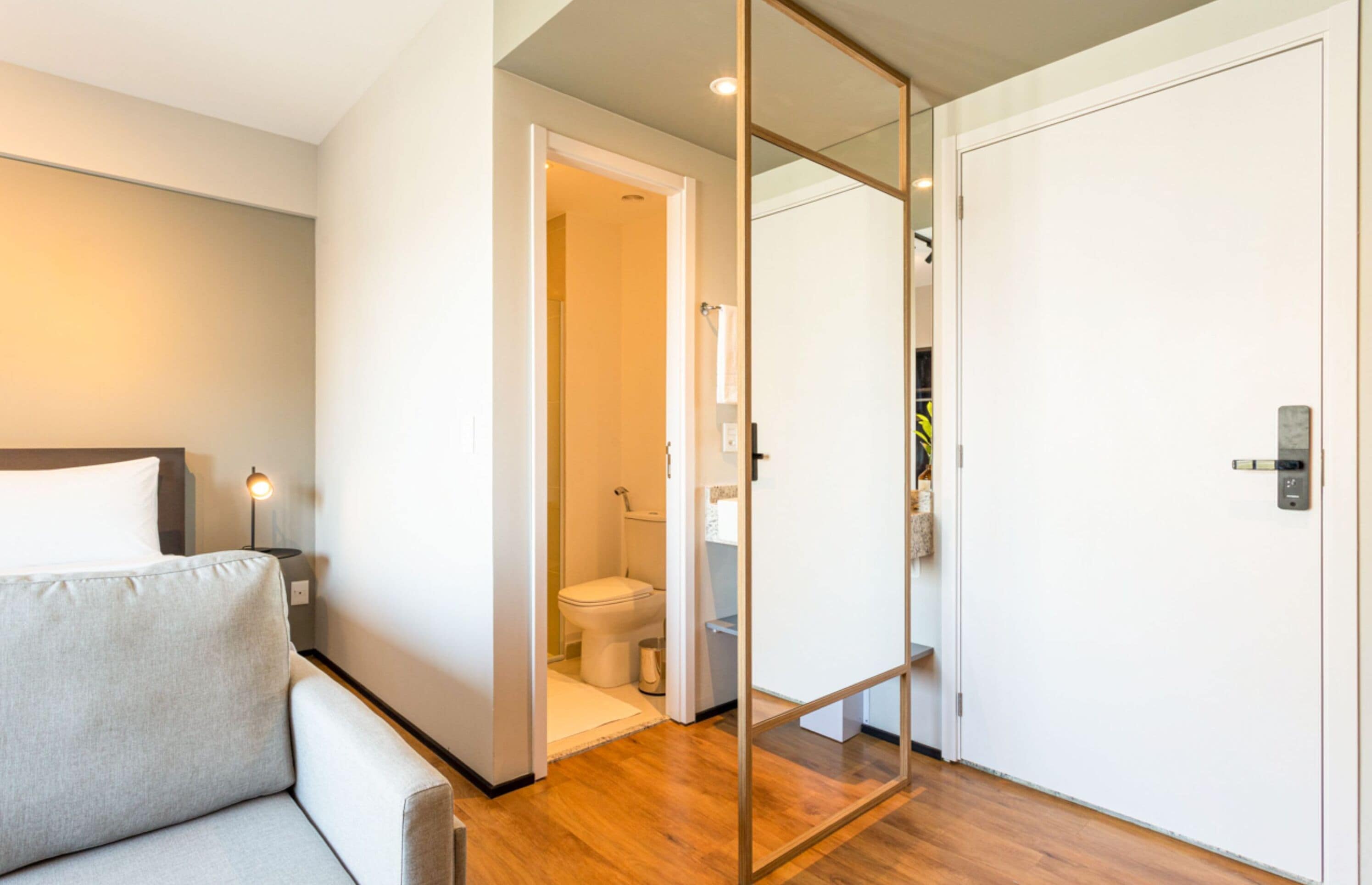 Une chambre d’hôtel moderne avec un canapé, une cloison en verre, un plancher en bois et une porte blanche.