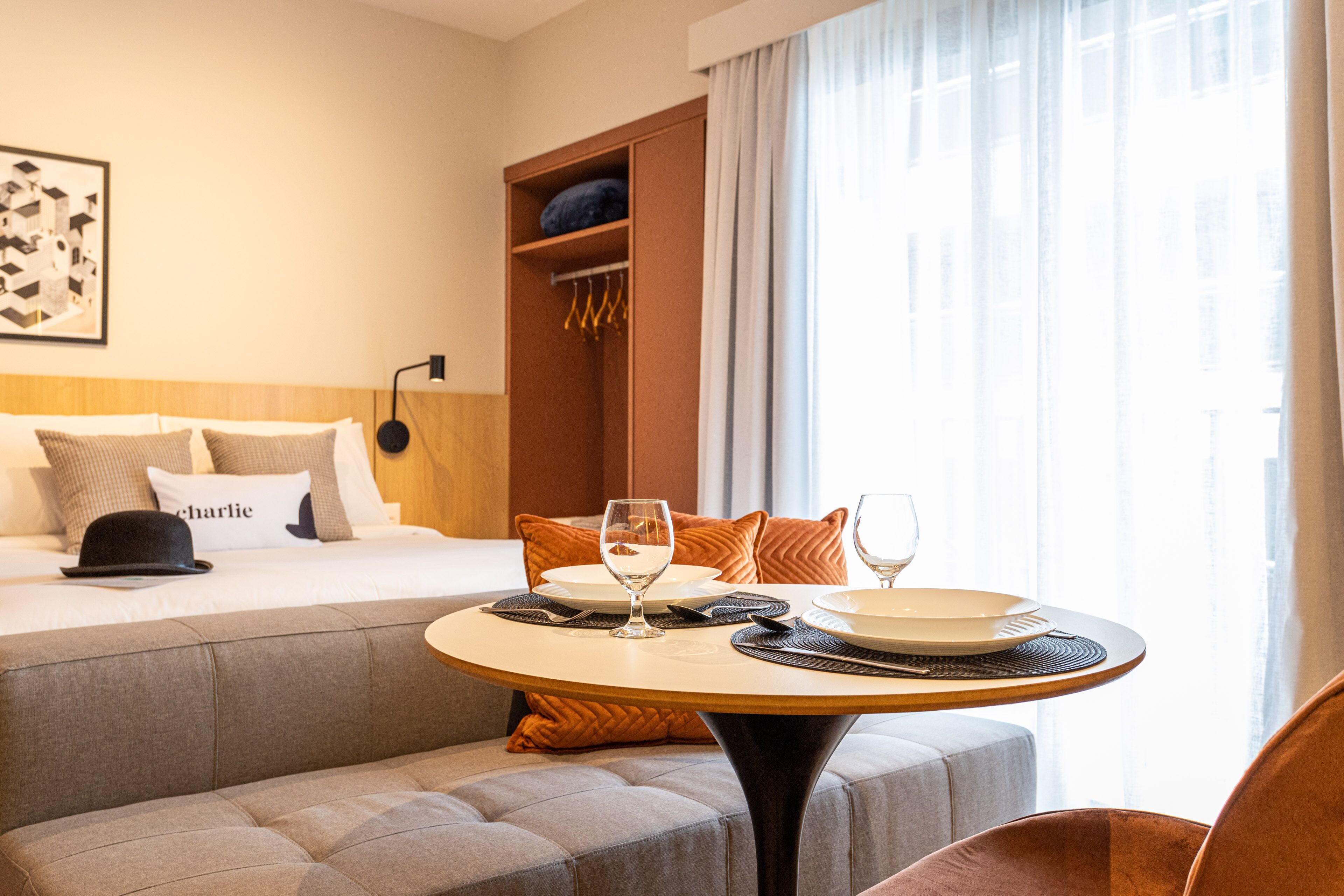 Une chambre d’hôtel comprenant un lit, une table ronde avec de l’assiette et des verres, un canapé et une armoire.