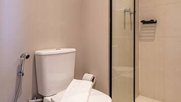 A modern bathroom with a toilet, a glass-enclosed shower, and a trash bin.