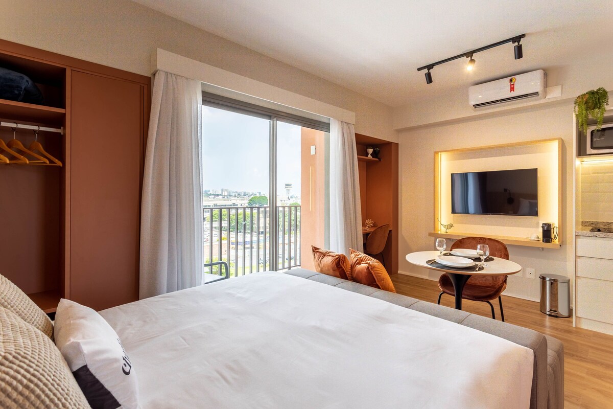 A hotel room with a large bed, a dining table with chairs, a TV, and a balcony with a view.