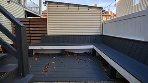 Una terrazza con una panca integrata, circondata da un recinto in legno e un edificio beige sullo sfondo.