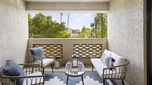 A balcony with wicker furniture, a glass table, and a view of greenery and buildings. - Biltmore Retreat Resort-Style Heated Pool Spa Gym (Phoenix)