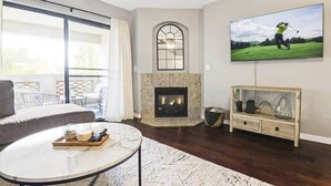 A living room with a fireplace, a television mounted on the wall, a sofa, and a coffee table. - Biltmore Retreat Resort-Style Heated Pool Spa Gym (Phoenix)