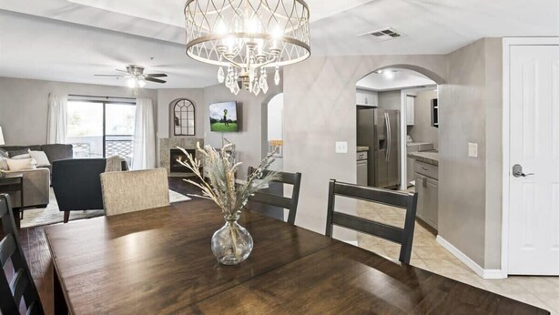 A modern dining area with a wooden table, chairs, a chandelier, and a vase with dried plants. - Biltmore Retreat Resort-Style Heated Pool Spa Gym (Phoenix)