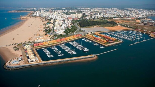 Vista aérea de una ciudad costera con un puerto deportivo, playa y edificios residenciales.