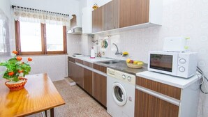 Una cocina compacta con armarios de madera, lavadora, microondas y pileta.