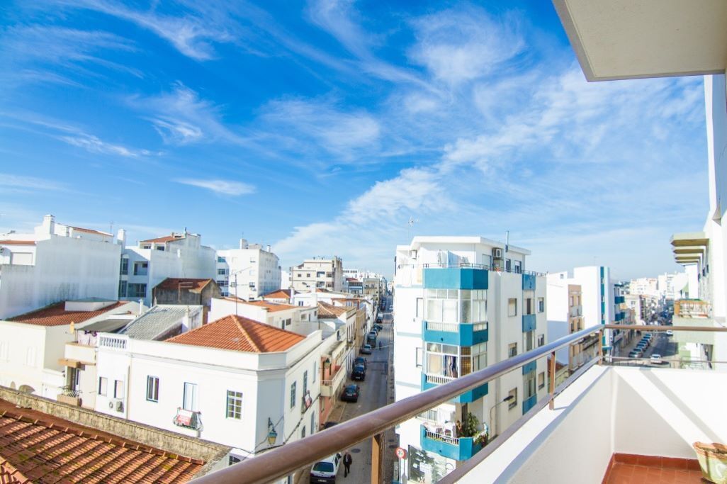 A cityscape with buildings, a clear sky, and a balcony with a railing.